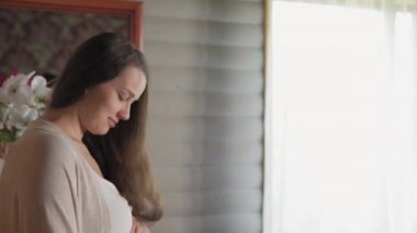 Mutlu doğal güzellik makyajsız hamile kadın pencerenin yanında karnına dokunuyor. Şefkatli anne, elleri aydınlatma odasında geniş karnını okşar. hamilelik, annelik, insanlar, beklenti kavramı