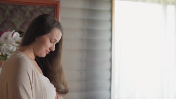 Feliz belleza natural mujer embarazada sin maquillaje tocando barriga en casa cerca de la ventana. madre cariñosa acaricia gran vientre con las manos en el espacio de luz. embarazo, maternidad, personas, concepto de expectativa — Vídeo de stock