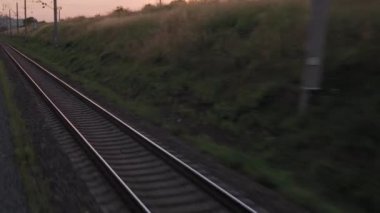Pencereden yüksek hızlı tren manzarası güzel doğa manzarası vahşi arazi ve orman rayları yaz arkaplanında akşam günbatımında tren rayları. Ulaşım, seyahat, demiryolu, iletişim konsepti