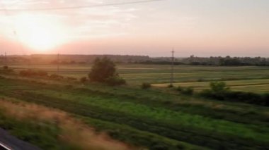 Pencereden yüksek hızlı tren manzarası güzel doğa manzarası vahşi arazi ve orman rayları yaz arkaplanında akşam günbatımında tren rayları. Ulaşım, seyahat, demiryolu, iletişim konsepti