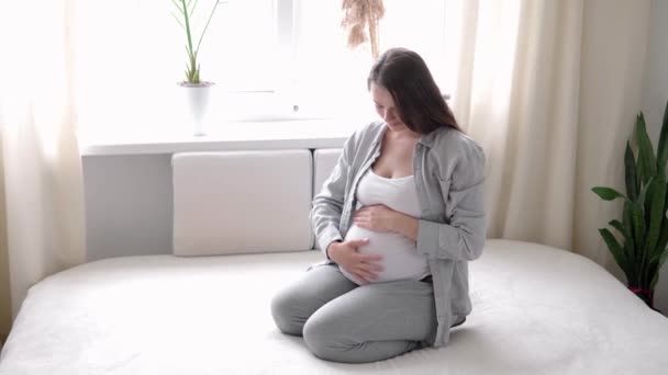 Zwangerschap, moederschap, mensen, verwachting concept - gelukkige zwangere vrouw aanraken van haar buik in bed thuis zorgzame moeder streelt naakt grote buik buik met handen, op lichte kamer in zonnige zomerdag — Stockvideo