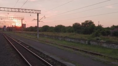 Pencereden yüksek hızlı tren manzarası güzel doğa manzarası vahşi arazi ve orman rayları yaz arkaplanında akşam günbatımında tren rayları. Ulaşım, seyahat, demiryolu, iletişim konsepti