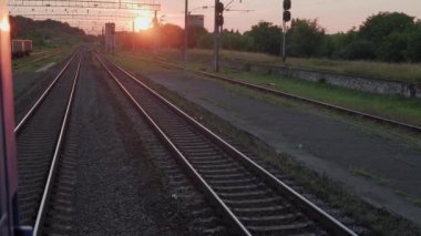 Pencereden yüksek hızlı tren manzarası güzel doğa manzarası vahşi arazi ve orman rayları yaz arkaplanında akşam günbatımında tren rayları. Ulaşım, seyahat, demiryolu, iletişim konsepti