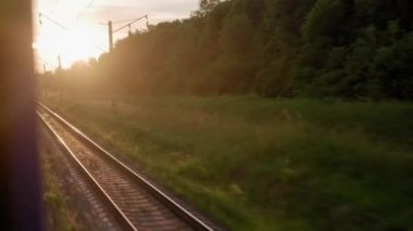 Pencereden yüksek hızlı tren manzarası güzel doğa manzarası vahşi arazi ve orman rayları yaz arkaplanında akşam günbatımında tren rayları. Ulaşım, seyahat, demiryolu, iletişim konsepti