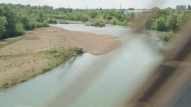 Köprüden ve orman demiryollarından güzel doğa nehrinin manzarasına bakan yüksek hızlı trenden manzara yaz arka planında güneşli bir gün. Ulaşım, seyahat, demiryolu, iletişim konsepti