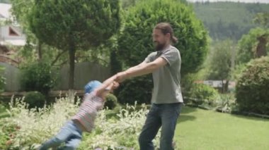 Neşeli Aile Komik Babası sakallı Çocuklar Kollar Arasında Sallanıyor. Baba, anaokulu kızı ve oğlu güneşli yaz gününde Idyllic Banliyö Evinin arka bahçesinde oyun oynuyorlar.