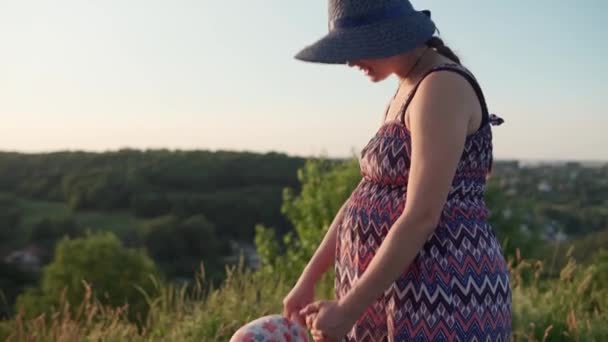 Linda mujer embarazada joven en sombrero de vestido largo con niña en la cima de la montaña antes del atardecer. gente en el parque. feliz mamá e hija bebé tomados de la mano. infancia, naturaleza, estilo de vida, concepto de verano — Vídeo de stock