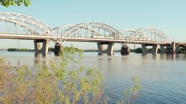 Ver la pesca en movimiento velero a motor en el río Dnipro al atardecer. paisaje de puente industrial sobre lago en ciudad. tren de pasajeros pasa sobre el estanque en el soleado día de verano el transporte de agua, viajes — Vídeos de Stock