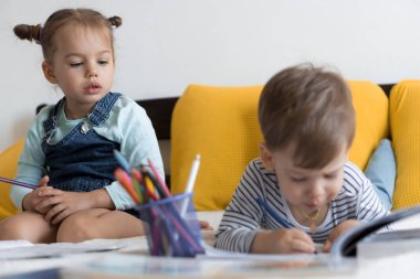 Zeki, gülümseyen, küçük bir çocuk çocuk ve kız sarı yatakta göbeklerinde kalemlerle resim yapıyorlar. Küçük sevimli okuyucu evde karantinada eğleniyor, mutlu çocuk. Arkadaşlık, aile, eğitim.