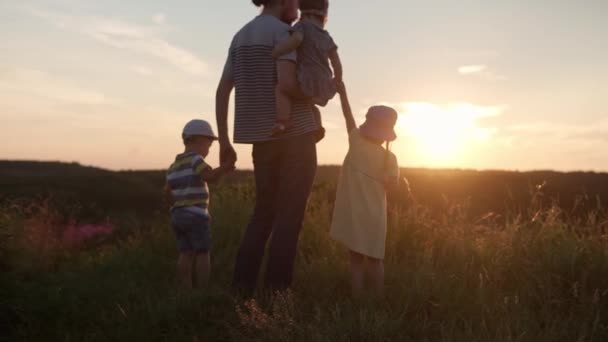 Gente en el parque. feliz caminata familiar en el campo. papá con muchos niños en la cima de la montaña en la hierba alta antes del atardecer. padres y niños divertidos miran a la distancia. verano, paternidad, concepto de infancia — Vídeos de Stock