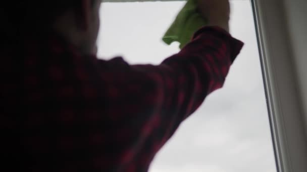 Mytí skla doma. Mladý dlouhosrstý muž s vousy uklízí byt. Sanitární pracovník dezinfikuje panoramatická okna v prázdné místnosti. čistota, čistota, změna koncepce — Stock video