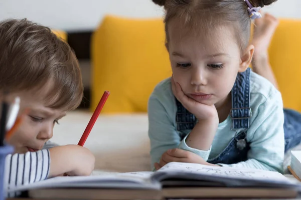 Intelligent souriant préscolaire tout-petit enfants garçon et fille dessiner avec des crayons couchés sur le ventre au lit jaune. petit lecteur mignon amusez-vous, enfant heureux en quarantaine à la maison. Amitié, famille, éducation — Photo