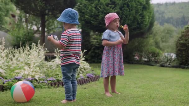 Happy Cute Children blowing soap bubbles. Preschool Boy and Girl Daughter and Son Have Fun Playing Games in the Backyard Lawn of Idyllic Suburban House on Sunny Summer Day. Childhood, family concept — Stock Video
