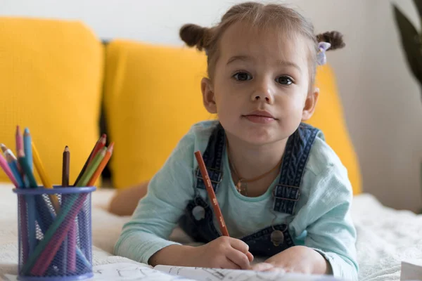 Slimme glimlachende preshool peuter kinderen jongen en meisje tekenen met potloden liggend op hun buik op geel bed. kleine schattige lezer veel plezier, gelukkig kind op quarantaine thuis. Vriendschap, familie, opvoeding — Stockfoto