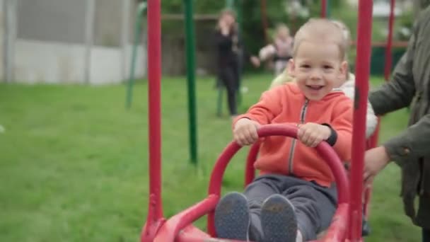 Carino graziosi bambini in età prescolare con la giovane mamma giocherellare in treno swing sul parco giochi. Piccolo bambino ridendo divertirsi, oscillando su altalena gioco da tavolo. Concetto di infanzia felice, emozioni positive, POV — Video Stock