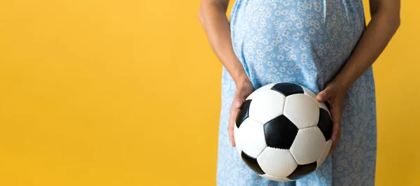 Motherhood, femininity, football, sport, dairy, hot summer. banner pregnant young pretty woman in floral blue dress holds soccer white and black leather classic ball rubs tummy on yellow background — Stock Photo, Image