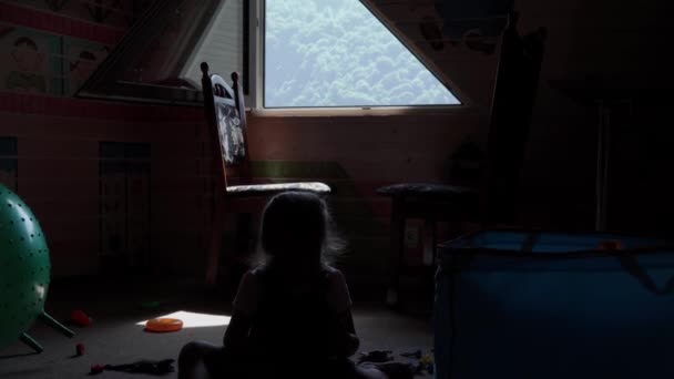 Silueta niña preescolar pequeña sentada en el suelo con juguetes en la habitación de los niños ventana opuesta con vista a las montañas. Los niños han pasado un tiempo divertido en casa. Infancia, amistad, concepto de desarrollo — Vídeo de stock