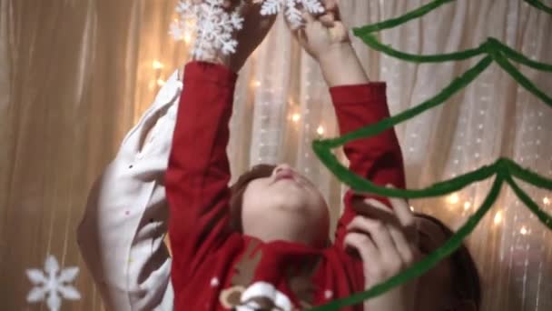 Auténtica mamá linda y dos niños pequeños preescolares hermanos niña y niño de 2-4 años dibujan el árbol de Navidad en la ventana. mujer joven con niños pega copos de nieve. Navidad, Año Nuevo, concepto de invierno. — Vídeos de Stock