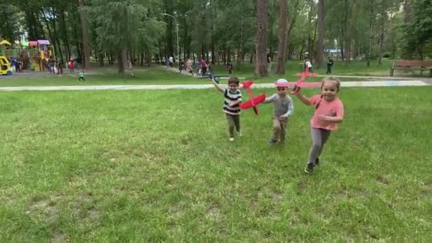 Tres felices hermanos preescolares niños niños amigos niños corriendo por ahí divertirse en el parque de verano jugando en el prado celebrar aviones de juguete lanzamiento volar al cielo. Infancia, amistad, descanso, naturaleza — Vídeos de Stock