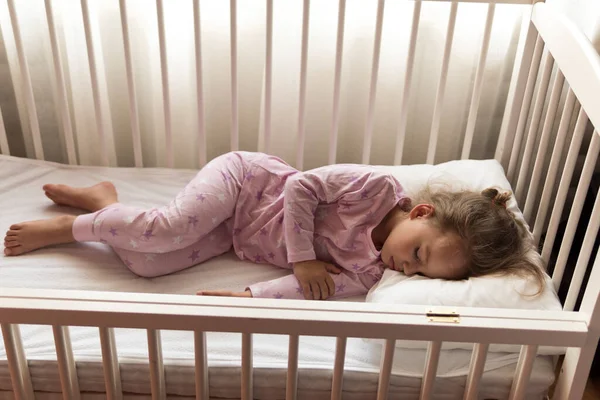 Arriba ver Lindo niño pequeño de 3-4 años de preescolar que duerme dulcemente en una cuna blanca durante el almuerzo, tiempo de descanso en pijama rosa con almohada en casa. Infancia, ocio, comodidad, medicina, concepto de salud — Foto de Stock