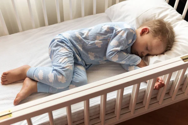 Arriba ver Lindo niño pequeño de 2-3 años de preescolar que duerme dulcemente en una cuna blanca durante el almuerzo, tiempo de descanso en pijama azul con almohada en casa. Infancia, ocio, comodidad, medicina, concepto de salud — Foto de Stock