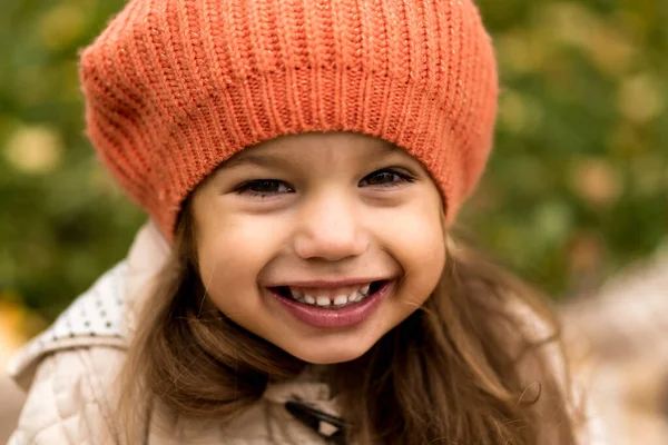 Primer plano Retrato de la pequeña niña preescolar linda en boina naranja en hojas caídas amarillas Niza sonriente mirando a la cámara en clima frío en el parque de otoño. Infancia, Familia, Maternidad, Concepto de otoño —  Fotos de Stock