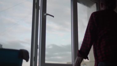 Evde cam silecekmiş. Uzun saçlı, sakallı genç bir adam daireyi temizliyor. Temizlik işçisi boş bir odadaki panoramik pencereleri dezenfekte ediyor. saflık, temizlik, konsepti değiştirme.