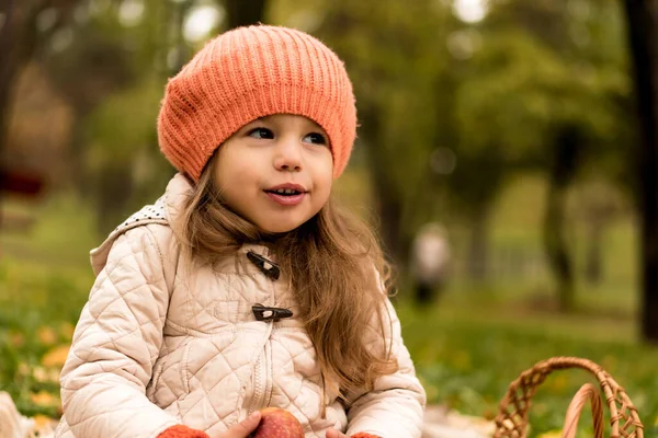 Κοντινό πλάνο Πορτρέτο Μικρό χαριτωμένο κορίτσι προσχολικής ηλικίας σε πορτοκαλί μπερέ σε κίτρινο πεσμένο φύλλα τρώει κόκκινο μήλο ονειροπολεί κοιτάζει μακριά. Κρύο καιρό στο Φολ Παρκ. Παιδική ηλικία, Οικογένεια, Μητρότητα, Φθινόπωρο Έννοια — Φωτογραφία Αρχείου