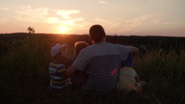 公园里的人快乐的家人在田里散步。日落前，爸爸带着许多孩子在山顶的高高的草地上。父母和有趣的孩子从远处看去。夏天、父亲、童年的概念 — 图库视频影像