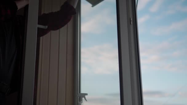 Fensterglas zu Hause waschen. Ein junger langhaariger Mann mit Bart putzt gerade die Wohnung. Sanitäter desinfizieren in einem leeren Raum Panoramafenster. Reinheit, Sauberkeit, Veränderungskonzept — Stockvideo