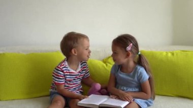 İki Gülen Anaokulu Çocuğu Koltukta Masal Kitabı 'nı okuyor. Kardeşler birbirlerine bakar ve öpüşürler. - Evet. Evdeki karantinada mutlu çocuk. Arkadaşlık, Aile, Eğitim