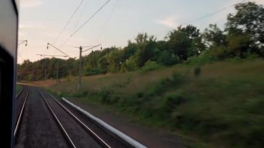 Pencereden yüksek hızlı tren manzarası güzel doğa manzarası vahşi arazi ve orman rayları yaz arkaplanında akşam günbatımında tren rayları. Ulaşım, seyahat, demiryolu, iletişim konsepti