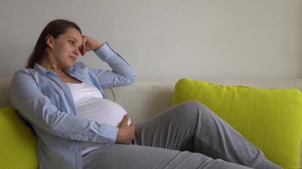Söt gravid kvinna stroke stora magen vidrör magen i solig dag. Ung Ledy i graviditeten ha kul tillbringa tid på gul soffa hemma. Moderskap, föräldraskap, medicin Hälsa och omsorg prenatal — Stockvideo