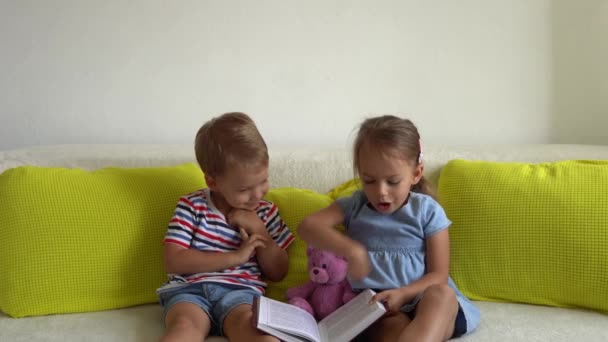 两个可爱的长颈鹿小孩在沙发上看《童话书》。姐妹俩在索法上花了不少时间。快乐的孩子在家里检疫。友谊、家庭、教育、重返校园 — 图库视频影像