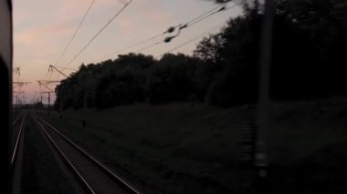 Pencereden yüksek hızlı tren manzarası güzel doğa manzarası vahşi arazi ve orman rayları yaz arkaplanında akşam günbatımında tren rayları. Ulaşım, seyahat, demiryolu, iletişim konsepti