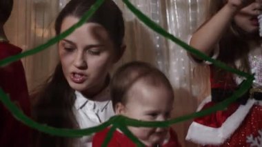 Otantik sevimli bir anne ve iki küçük anaokulu öğrencisi kız ve erkek kardeş 2-4 yaşlarında pencereye Noel ağacı çiziyor. Çocuklu genç bir kadın kar taneleri yapıştırıyor. Xmas, yeni yıl, kış konsepti.