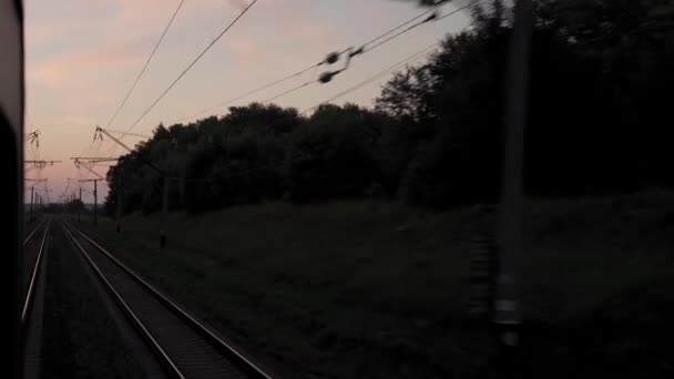 Vista da janela de trem de alta velocidade na paisagem da bela natureza campo selvagem e trilhos ferroviários florestais no pôr do sol da noite em fundo de verão. Transporte, viagens, ferrovia, conceito de comunicação — Vídeo de Stock