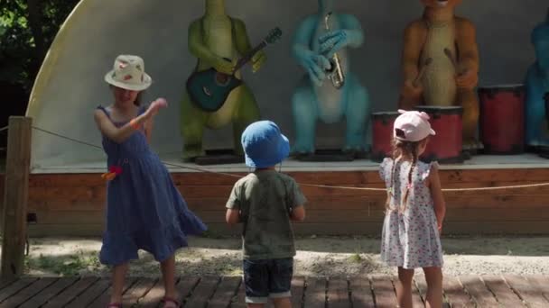 2021.08.12 - Kiev, Ucraina: I bambini ballano divertiti a passare del tempo vicino al palco con i dinosauri modello in movimento Musicisti Mockup. Vari animali motorizzati con strumenti musicali Depict Rosk Group a Dinopark — Video Stock