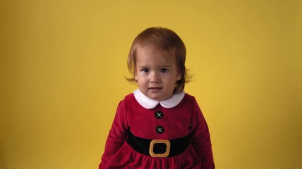 Cute Happy Cheerful Chubby Toddler Baby Girl in Santa Suit Looking On Camera At Yellow Background Діти грають різдвяну сцену, святкуючи день народження. Дитячі забави витрачаються на Новий рік. Дитинство — стокове відео