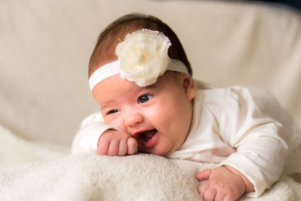 Gyermekkor, anyaság, érzelmek, divat fogalmak - Aranyos mosolygós boldog pufók baba közelről kislány gyönyörű fehér ruha virág fejpánt fején fekvő puha meleg ágy a has otthon — Stock Fotó