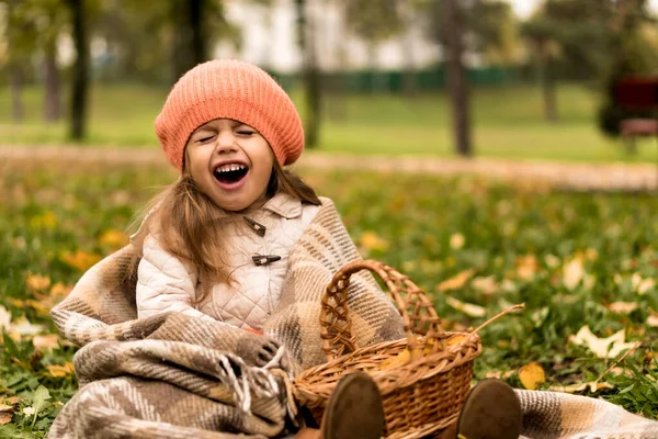 Μικρό χαριτωμένο Νηπιαγωγείο κορίτσι σε πορτοκαλί μπερέ σε θέση σε κίτρινο πεσμένα φύλλα σε καλάθι γελάει πλατιά χαμογελώντας κλειστά μάτια σε κρύο καιρό στο πάρκο πτώση. Παιδική ηλικία, Οικογένεια, Μητρότητα, Φθινόπωρο Έννοια — Φωτογραφία Αρχείου