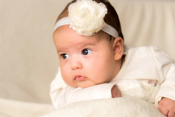 Παιδική ηλικία, μητρότητα, συναισθήματα, έννοια της μόδας - ανησυχούν θλιβερό κλάμα παχουλό μωρό με ανοιχτό το στόμα close up κοριτσάκι στο όμορφο λευκό φόρεμα floral κεφαλόδεσμο που βρίσκεται στο μαλακό ζεστό κρεβάτι στην κοιλιά στο σπίτι — Φωτογραφία Αρχείου