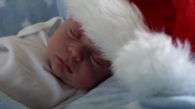 Hayatın ilk günleri yakın plan, yeni doğan tatlı, komik, Noel Baba 'nın içinde uyuyan bebek, kırmızı şapkalı, mavi yıldızlı arka planda yatıyor. Mutlu Noeller ve mutlu yıllar, bebekler, çocuklar, tatiller