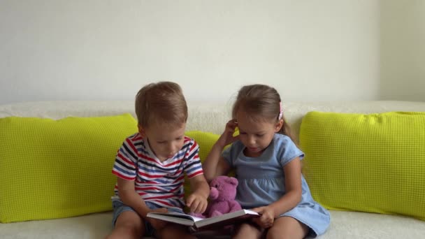 Duas crianças bonitos Preshool criança ler livro de contos de fadas no sofá. Os irmãos gêmeos divertem-se no sofá. Crianças felizes em quarentena em casa. Amizade, Família, Educação, De Volta à Escola — Vídeo de Stock