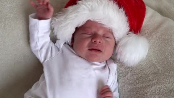 Feliz Natal e feliz ano novo, bebês, infância, conceito de férias - close-up vista superior primeiros dias de vida recém-nascido engraçado triste chorando bebê em Papai Noel chapéu vermelho na mentira em volta no fundo branco — Vídeo de Stock