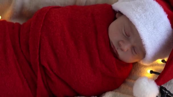 Yeni doğan bebeğin ilk portresi beyaz çelenk arka planında kırmızı beze sarılı, Noel Baba şapkalı komik uyuyan bebek. Mutlu Noeller, Mutlu yıllar, Bebek, Çocukluk, Kış Konsepti — Stok video