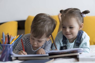 Zeki, gülümseyen, küçük bir çocuk çocuk ve kız sarı yatakta göbeklerinde kalemlerle resim yapıyorlar. Küçük sevimli okuyucu evde karantinada eğleniyor, mutlu çocuk. Arkadaşlık, aile, eğitim.