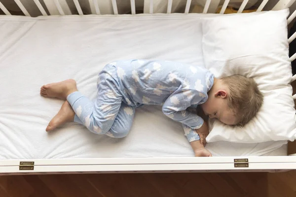 2-3 yaş arası, şirin, kreş çocuğu öğle yemeği arasında evinde yastıklı mavi pijamayla beyaz karyolada tatlı tatlı uyuyor. Çocukluk, rahatlık, rahatlık, ilaç, sağlık konsepti — Stok fotoğraf