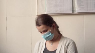 Genç Hamile Koruyucu Maskeli Kadın, hastane için randevu bekleyen koltukta kitap okuyor. Klinikteki jinekoloğu ziyaret et. Muayene Edilmeyi Bekleyen Göbek Sağlığı Kontrolü