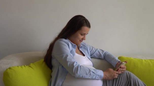 Щаслива вагітна жінка з планшетом має відеодзвінок за допомогою смартфона, який спілкується з чоловіком через онлайн-консультацію в чаті з лікарем, який спілкується з друзями на мобільному телефоні. вагітність, технології, медицина — стокове відео